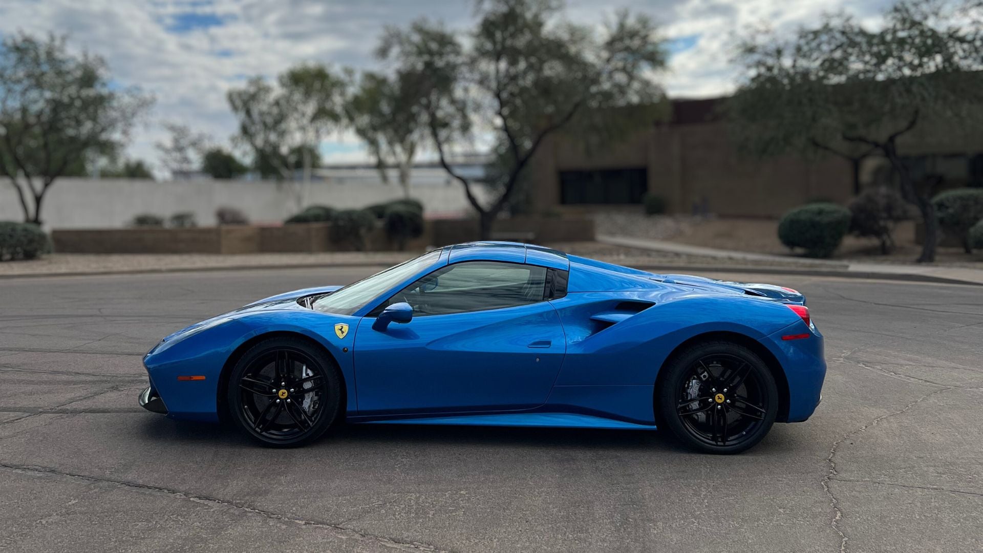 Blue Ferrari with paint protection film (PPF) and carbon fiber accents in Tempe AZ parked on a paved street with trees and buildings in the background