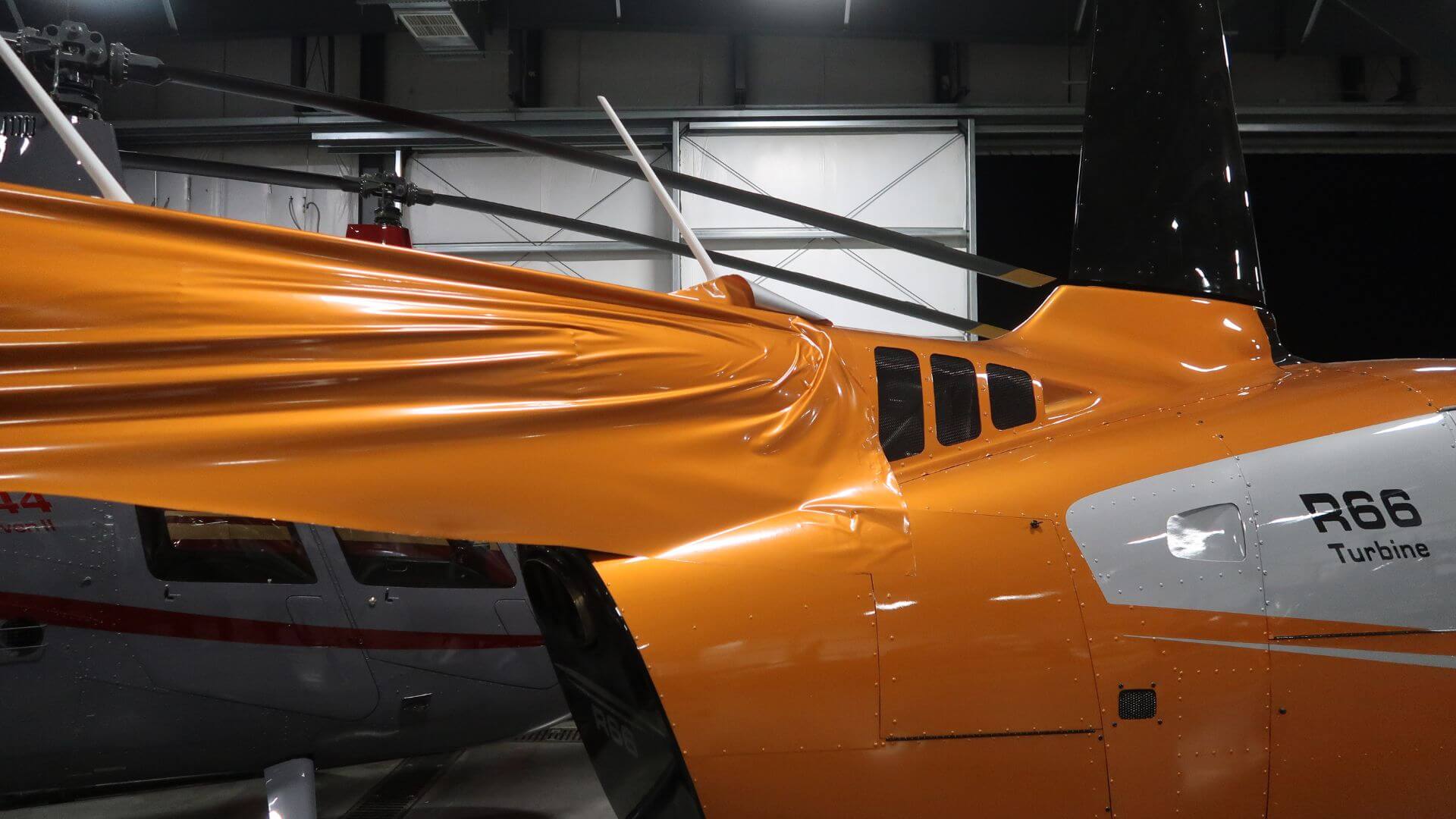 Robinson R66 helicopter being wrapped in orange liquid copper vinyl at Quantum Helicopters